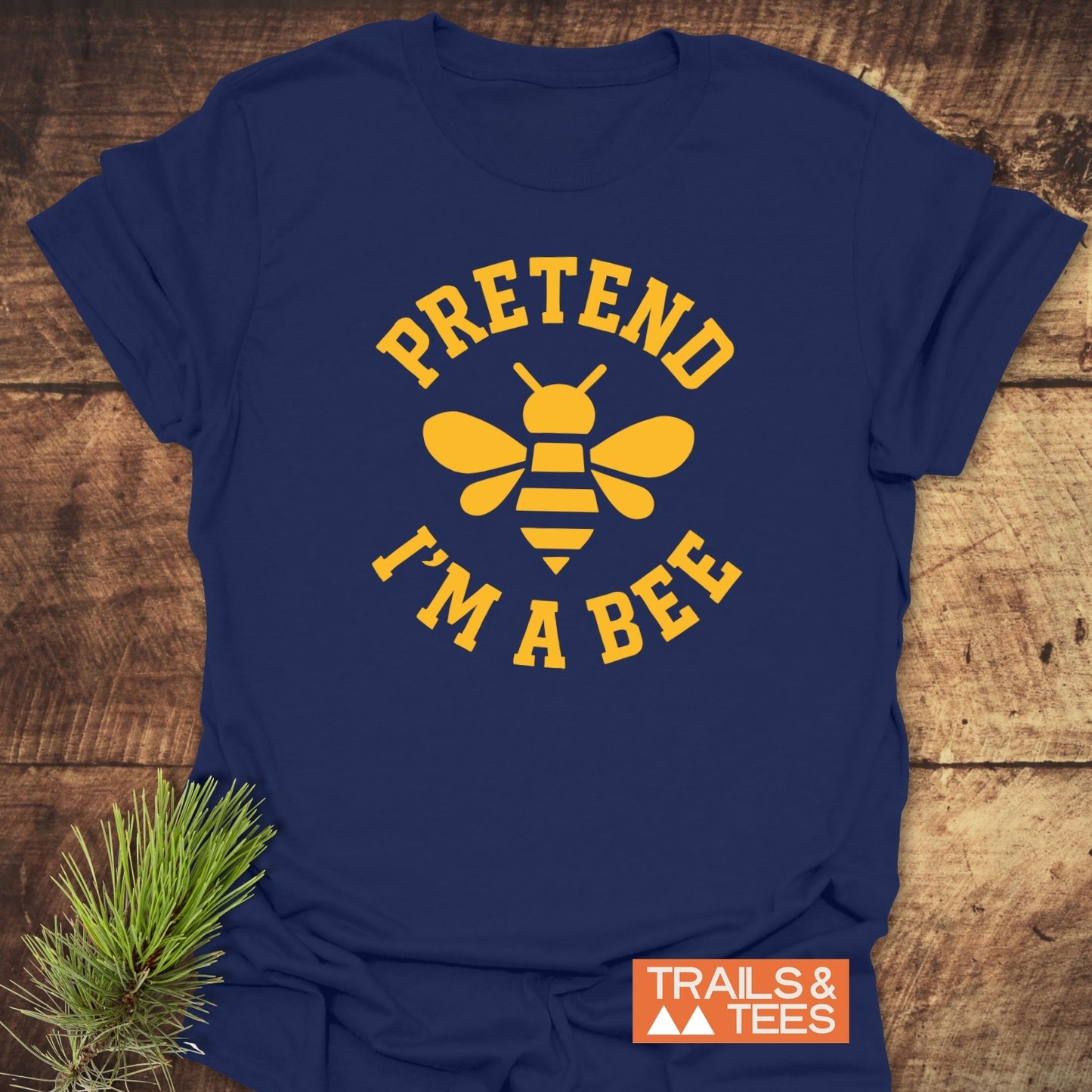 Navy-blue I'm A Bee Funny T-Shirt featuring a yellow bee graphic and text, laid on wood with a pine branch, Trails & Tees logo visible.