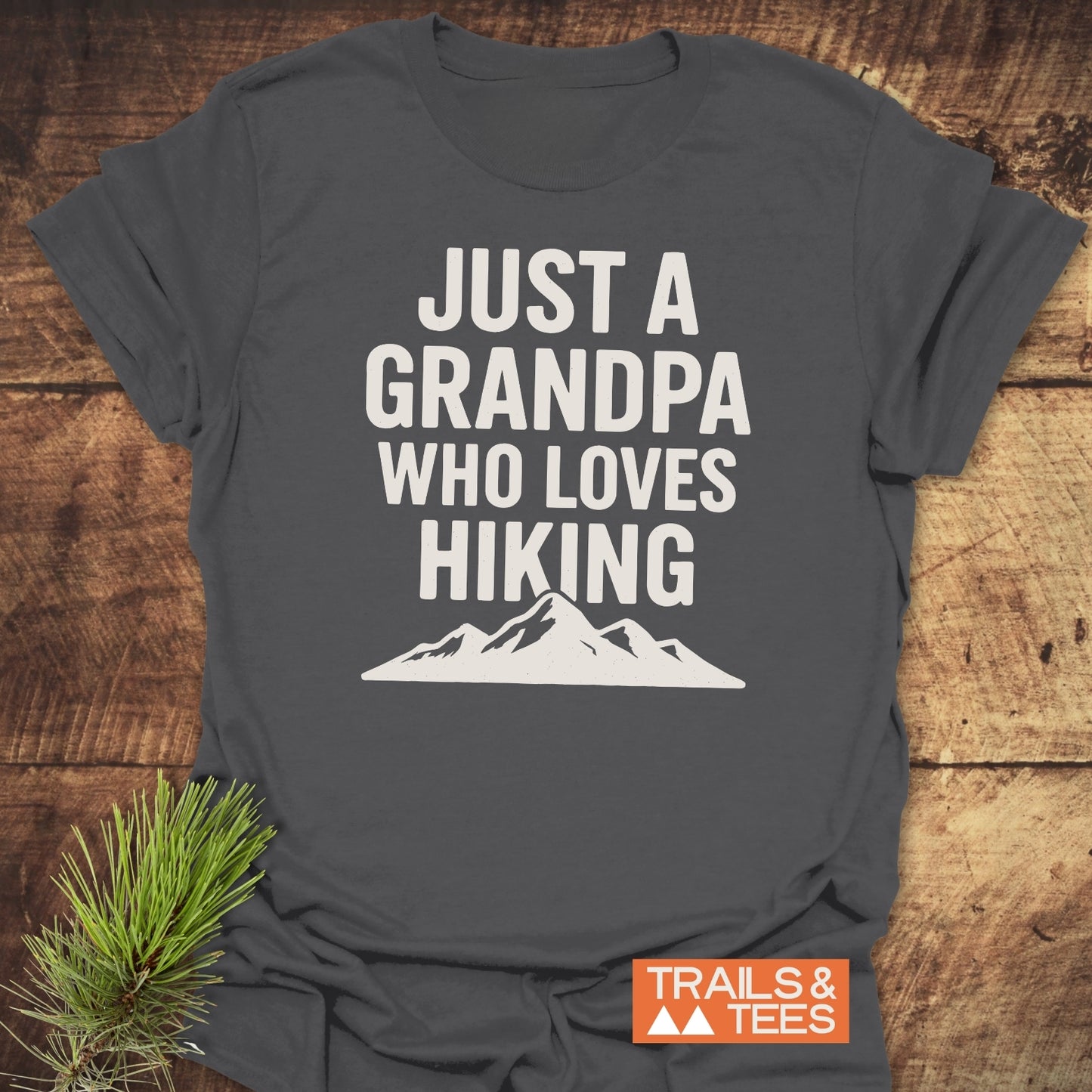 Hiking Grandpa T-Shirt featuring JUST A GRANDPA WHO LOVES HIKING slogan and mountain silhouette, highlighting comfort and durability with Trails & Tees logo.
