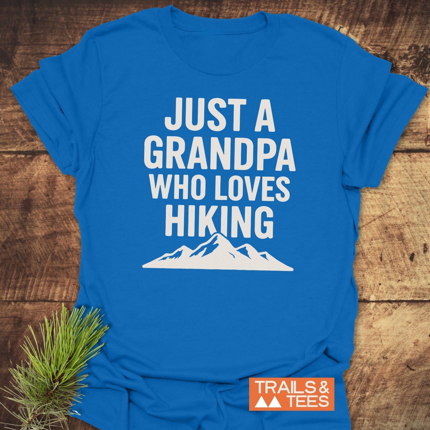 Hiking Grandpa T-Shirt with bold white slogan and mountain graphic on blue cotton, featuring a rustic pine accent and Trails & Tees logo.