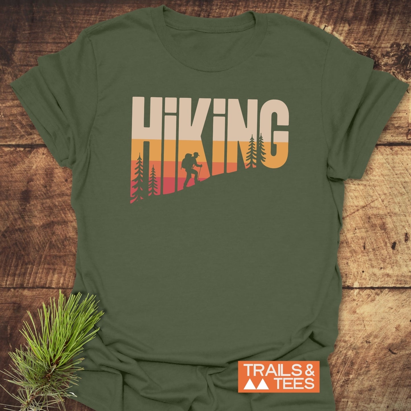 Olive-green Hiking Vintage T-Shirt with sunset-gradient hiking graphic, crafted from soft, lightweight cotton, laid on rustic wood, embodying outdoor adventure spirit.