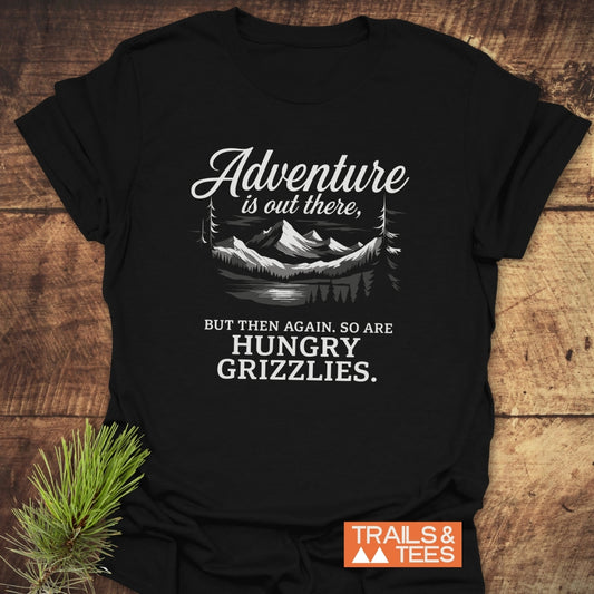 Adventure Is Out There T-Shirt featuring a mountain landscape graphic with slogan. Crafted from soft cotton, it offers comfort and durability for outdoor enthusiasts.