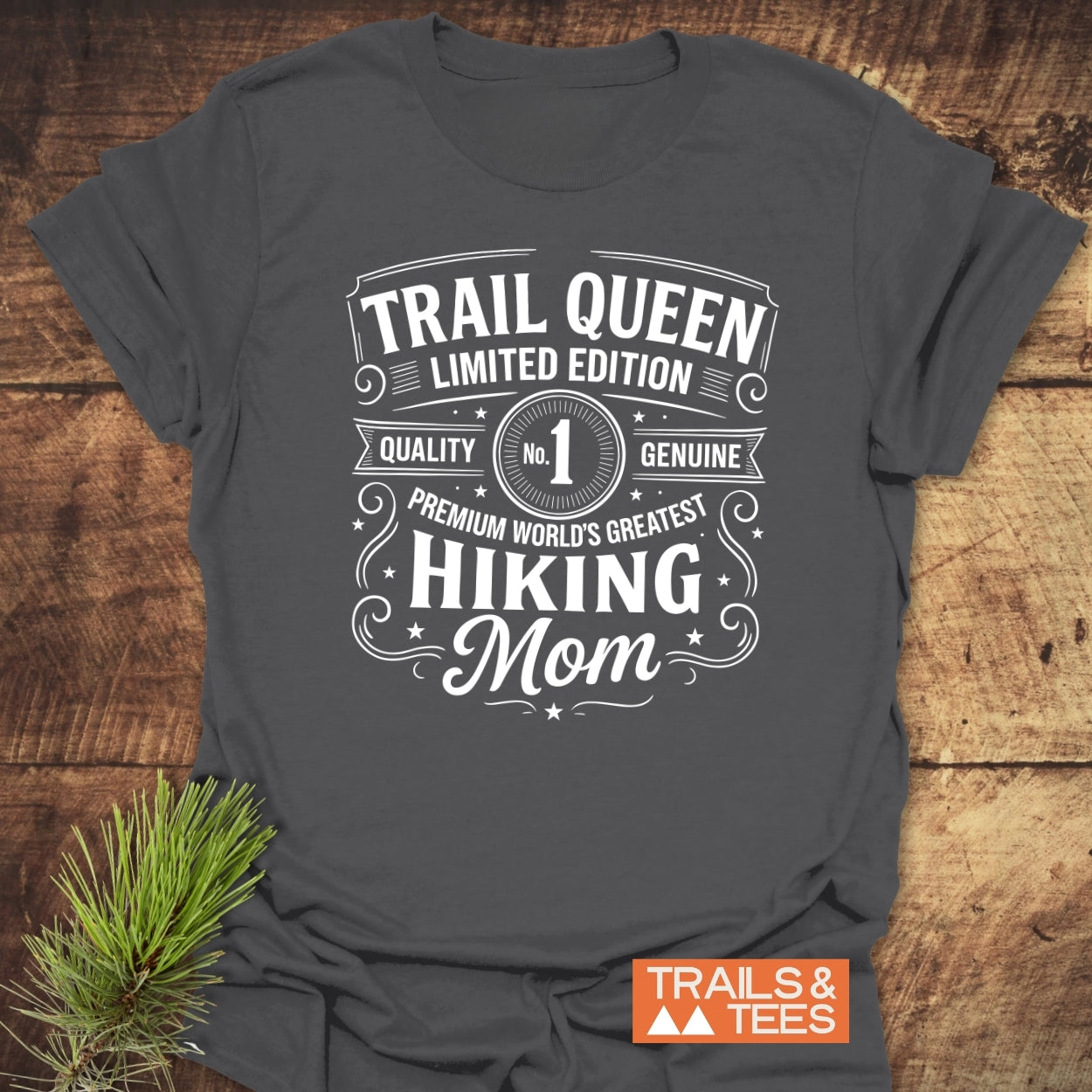 Charcoal-gray T-shirt with Trail Queen – Limited Edition white vintage design, beside pine sprig, highlighting comfort and durable quality for outdoor-loving moms.