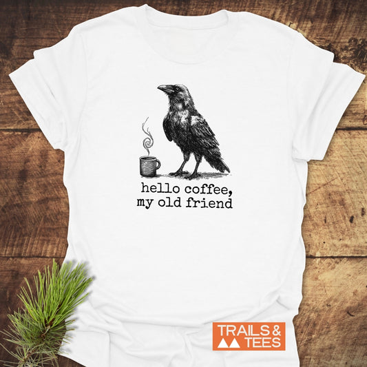 Flat-lay of Hello Coffee Funny T-Shirt featuring a raven with coffee mug sketch and typewriter-style text, ‘hello coffee, my old friend,’ on soft, durable cotton.