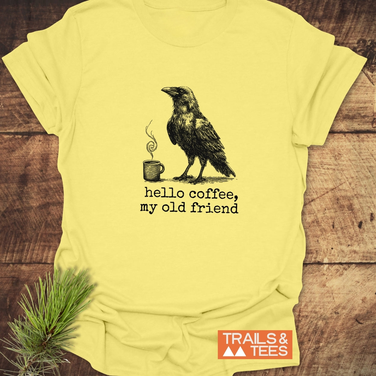 Hello Coffee Funny T-Shirt featuring a raven and coffee mug design, crafted from lightweight ring-spun cotton for comfort, with durable prints and a TRAILS & TEES logo.