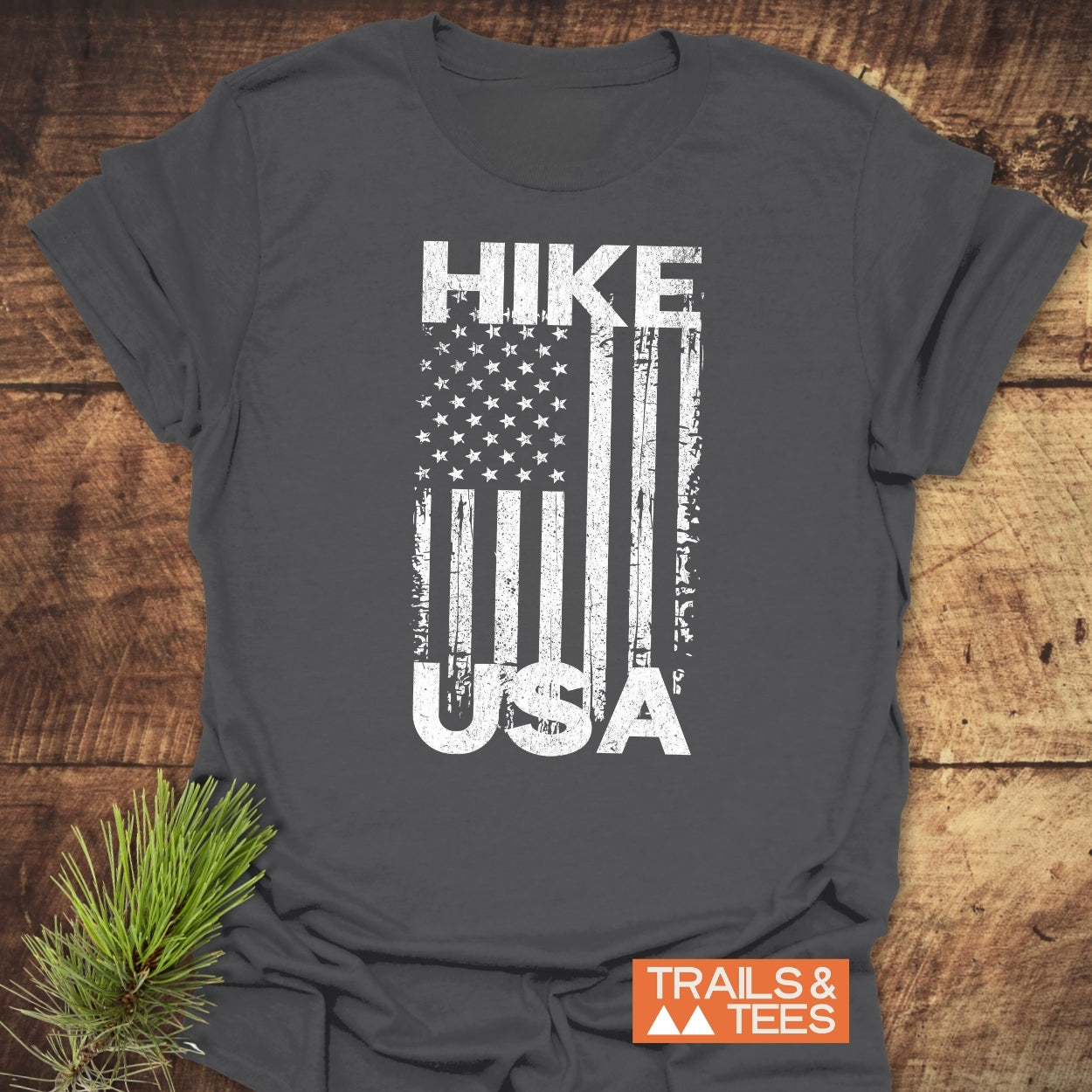 Hike USA T-Shirt with distressed American flag design, crafted from soft ring-spun cotton, laid flat with a pine sprig beside it.