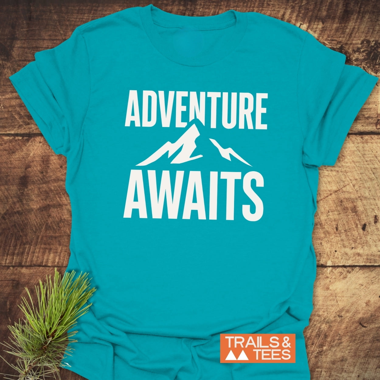 Adventure Awaits T-Shirt with mountain graphic and “TRAILS & TEES” logo, crafted from soft cotton for comfort, ideal for outdoor enthusiasts.