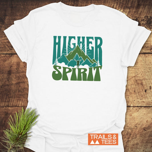 Higher Spirit T-Shirt featuring green mountain graphic and HIGHER SPIRIT text, laid on wood surface with pine branch, emphasizing outdoor adventure and comfort.