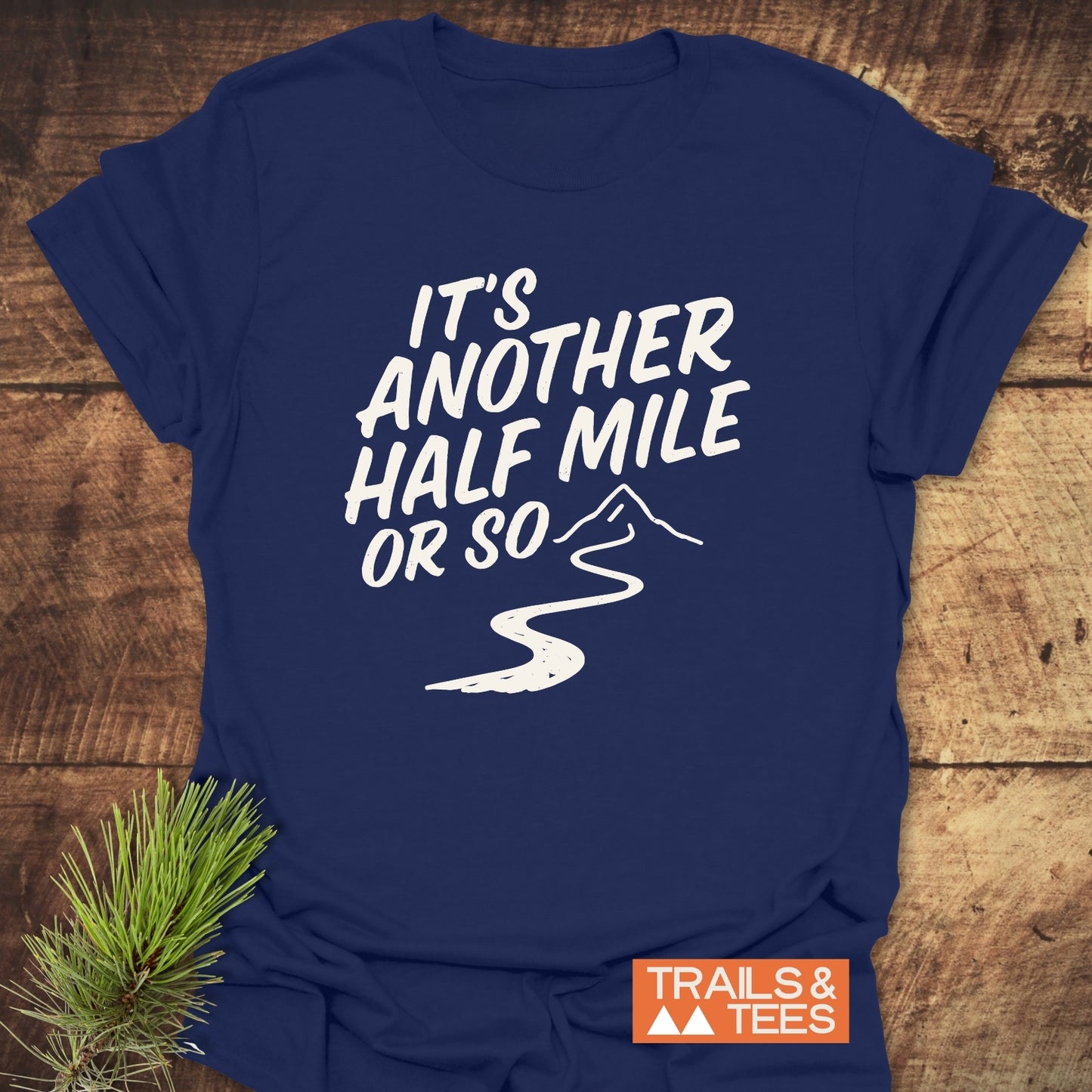 Half Mile Funny T-Shirt with mountain trail graphic and slogan, “It’s another half mile or so,” on soft, ring-spun cotton, ideal for outdoor enthusiasts.