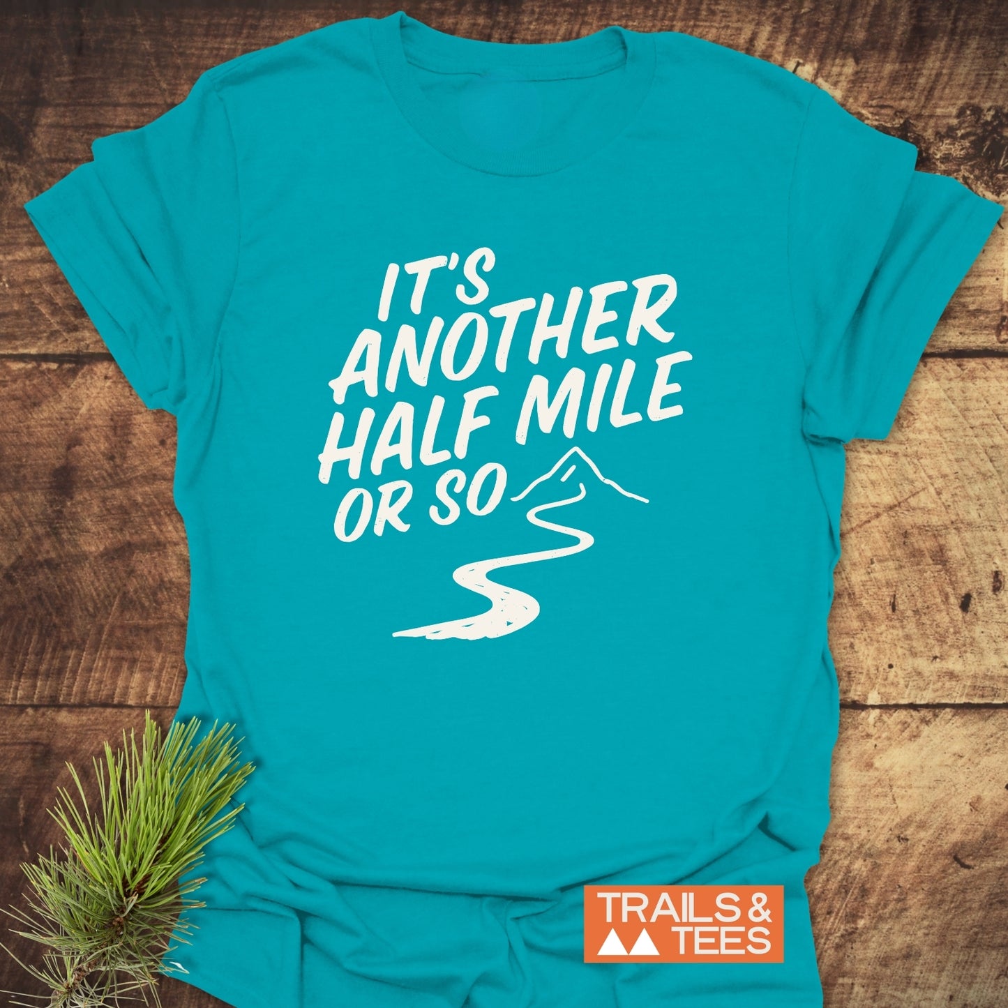 Half Mile Funny T-Shirt with “IT’S ANOTHER HALF MILE OR SO” print and mountain trail graphic, showcasing outdoor adventure theme; features durable, comfortable, pre-shrunk cotton.