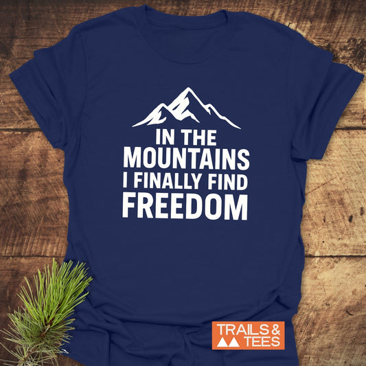 Finally Freedom T-Shirt with mountain graphic and quote, laid on wood surface. Features soft ring-spun cotton, durable prints, and is nature-inspired.