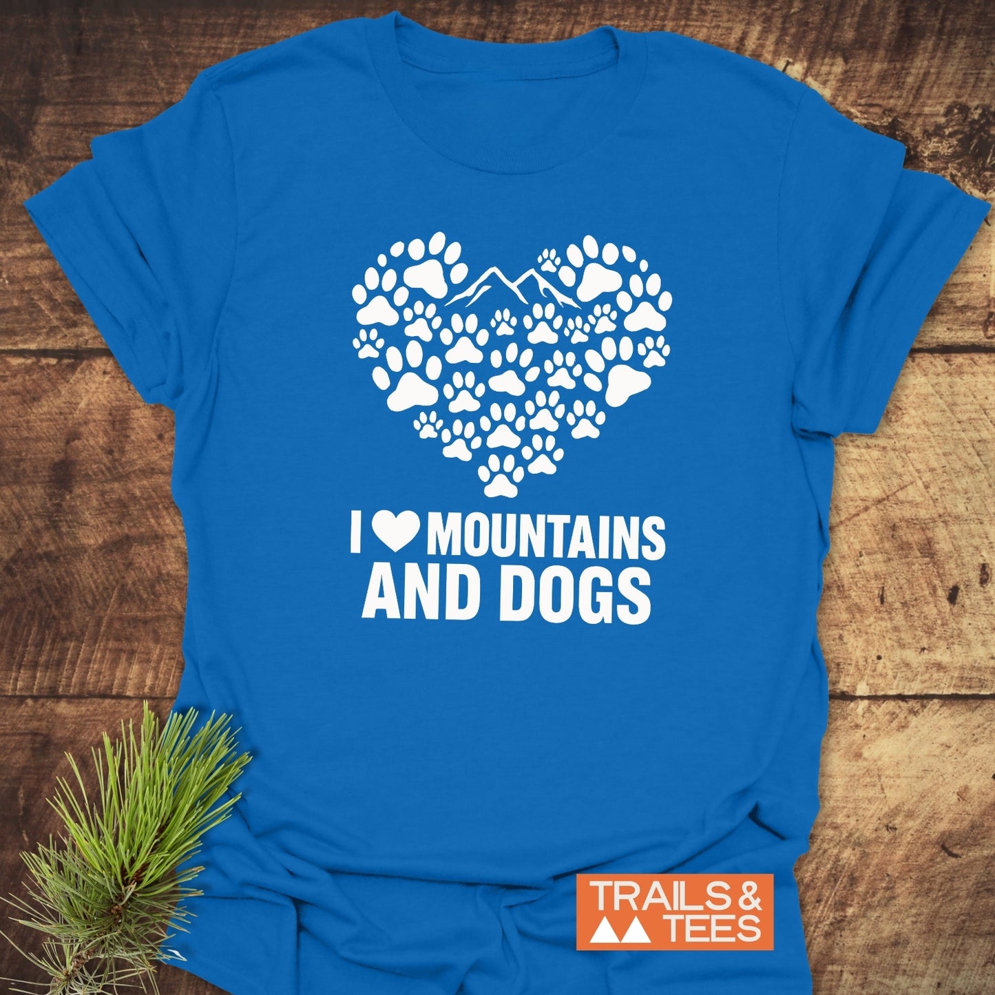 Paw Heart Dog Lover T-Shirt featuring a heart of paw prints with mountain peaks, slogan “I ♥ MOUNTAINS AND DOGS,” and “TRAILS & TEES” logo beside evergreen sprig.