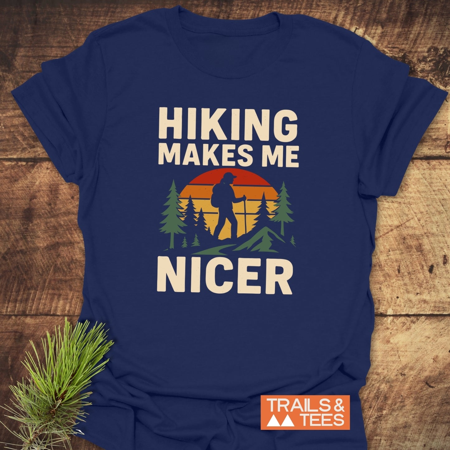 Hiking Makes Me Nicer T-Shirt: navy tee with hiker graphic, pine trees, sunset, and bold text, showcasing durable, lightweight, ring-spun cotton for outdoor enthusiasts.