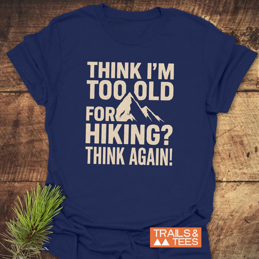 Navy-blue Think Again Funny T-Shirt with mountain graphic and bold text, featuring durable prints, on a wooden surface, adorned with a pine sprig.