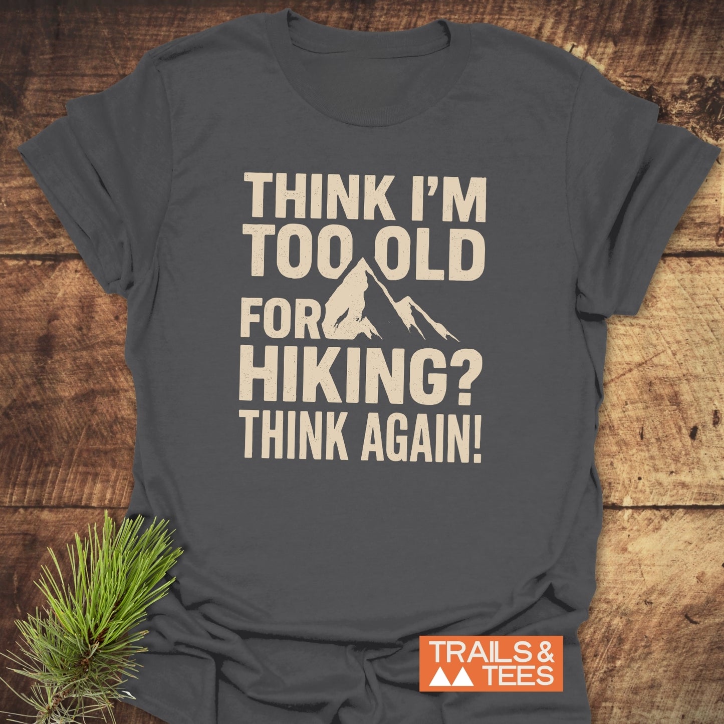 Slate-gray Think Again Funny T-Shirt with mountain peak print and slogan, folded on wood. Made from soft cotton, durable design by Trails & Tees.
