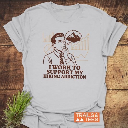 Hiking Addiction Funny T-Shirt featuring a retro man, charts, and mountain thought bubble, with slogan supporting hiking addiction. Includes Trails & Tees logo.