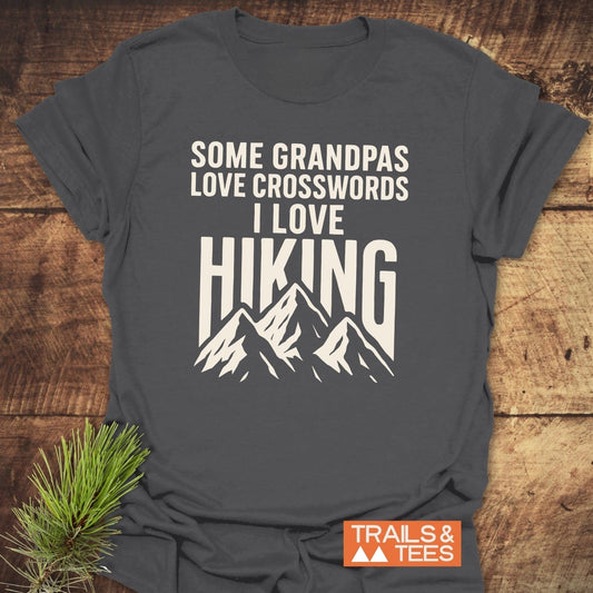 Grandpa Loves Hiking Funny T-Shirt in dark-gray with white text and mountain graphic, laid flat; soft, durable ring-spun cotton with Trails & Tees logo.