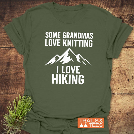 Hiking Grandma Funny T-Shirt with mountain graphic and slogan, showcased on wood. Features soft, ring-spun cotton for comfort, emphasizing outdoor adventure and sustainability.