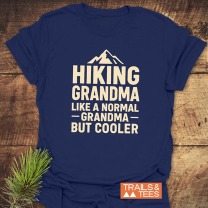 Navy-blue Hiking Grandma T-Shirt with mountain icon and slogan, laid on wood. Made from lightweight cotton, featuring durable print. Trail-tested comfort by Trails & Tees.
