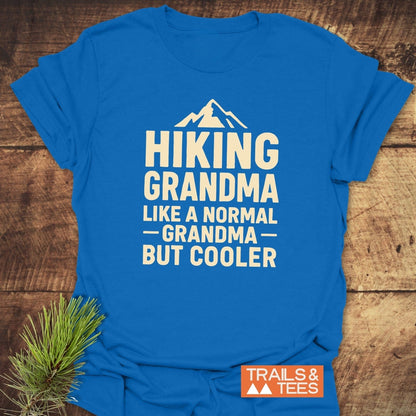 Hiking Grandma T-Shirt with mountain graphic, laid on wood. Cream print: “Hiking Grandma, Like a Normal Grandma, But Cooler.” Includes Trails & Tees logo.