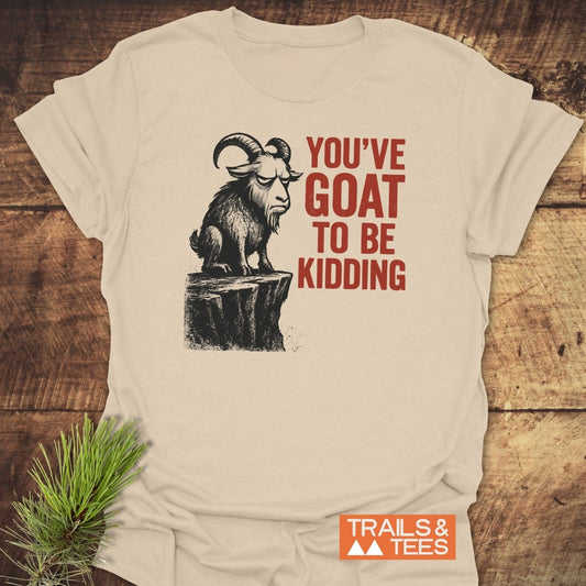 Kidding Goat Funny T-Shirt on wooden surface, features a goat graphic with bold red text. Includes TRAILS & TEES logo, emphasizing comfort and durability.