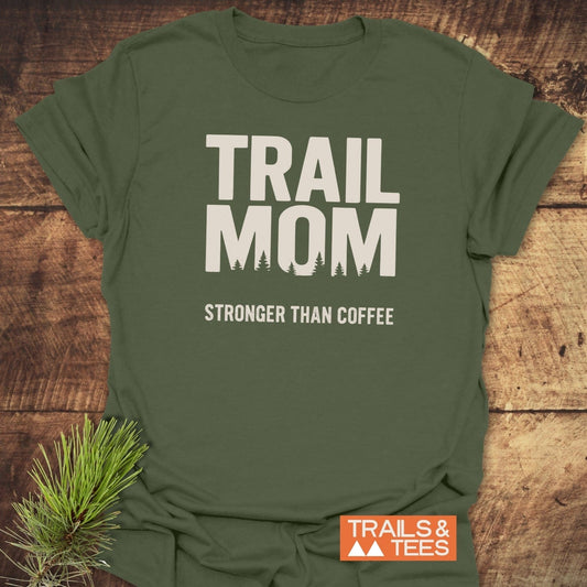 Mom Stronger Than Coffee T-Shirt with “TRAIL MOM” and tree silhouette design, featuring durable prints, laid on rustic wood with Trails & Tees logo.