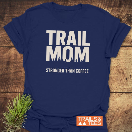 Navy-blue Mom Stronger Than Coffee T-shirt with a tree silhouette design, crafted from soft cotton, laid flat on a wooden surface with pine sprig.