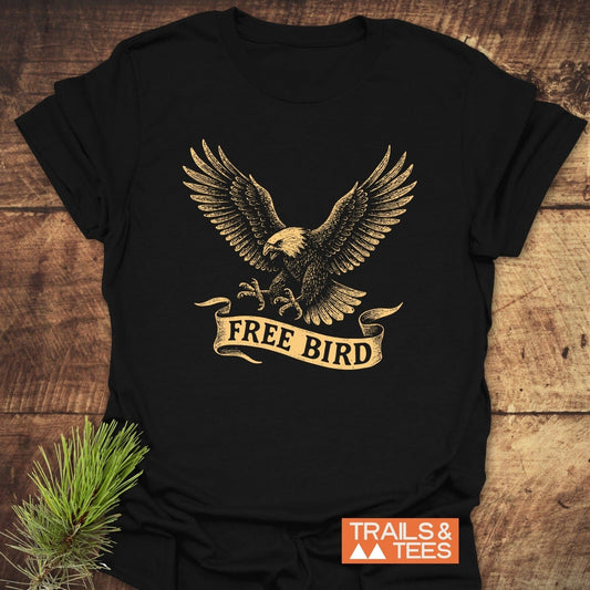 Free Bird T-Shirt featuring a vintage eagle graphic with FREE BIRD banner, laid on wood. Soft, durable cotton, perfect for outdoor adventures.
