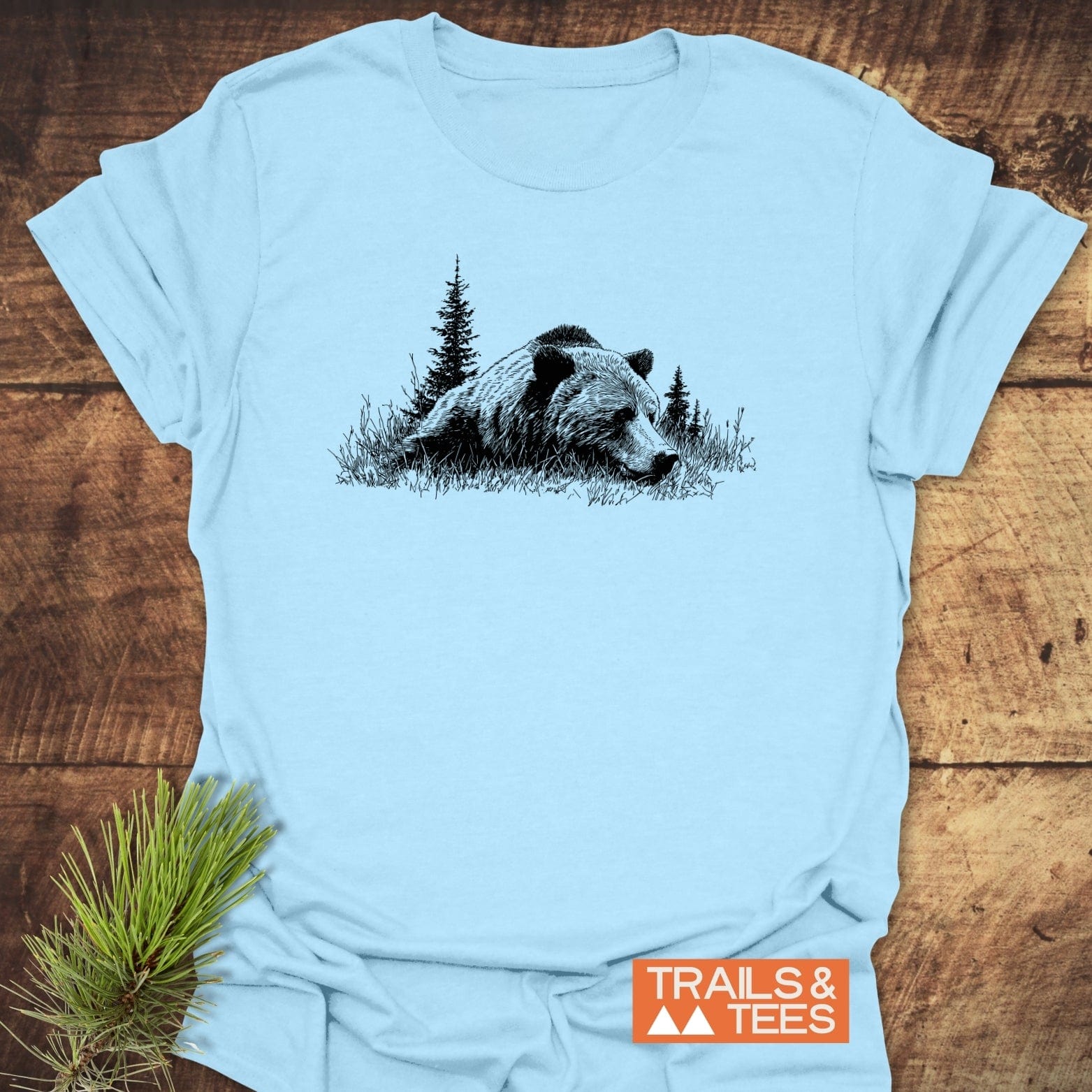 Relaxing Grizzly T-Shirt featuring a bear and pine trees design on soft ring-spun cotton, showcasing durability and outdoor-inspired comfort, with TRAILS & TEES logo.