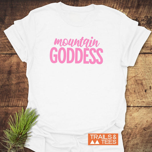 Mountain Goddess T-Shirt featuring pink lettering, displayed on wooden surface, highlights soft ring-spun cotton and durable design with Trails & Tees logo visible.