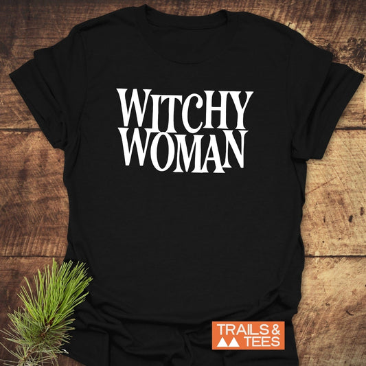 Witchy Woman T-Shirt on rustic wood, featuring bold white lettering. Made from soft, ring-spun cotton, perfect for outdoor adventures and everyday wear.
