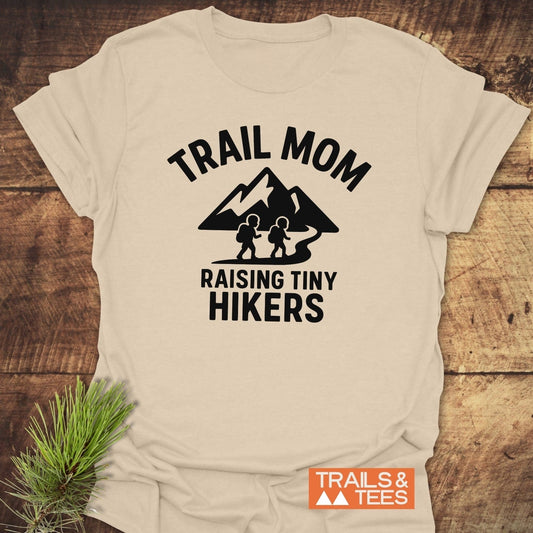 Raising Tiny Hikers Mom T-Shirt with TRAIL MOM graphic, mountain silhouette, and slogan. Soft ring-spun cotton, durable print, emphasizes outdoor adventures.