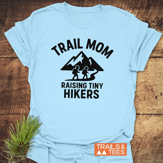 Raising Tiny Hikers Mom T-Shirt with backpacking figures and mountain graphic, promoting outdoor spirit. Soft, durable, pre-shrunk cotton for everyday adventure.