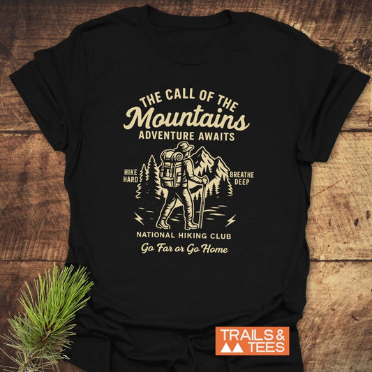 Call Of The Mountains T-Shirt: Black tee with cream hiker graphic and mountain scene, promoting adventure. Features durable print, soft cotton, no side seams.