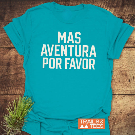 Mas Aventura T-Shirt with bold white text, laid on wood. Includes Trails & Tees logo. Crafted from soft, lightweight cotton for everyday adventure.