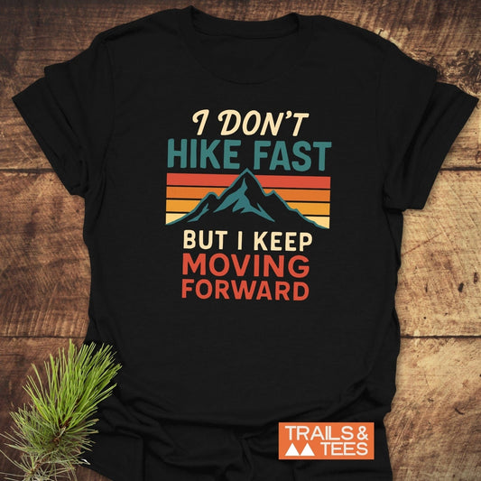 I Don't Hike Fast T-Shirt featuring a retro mountain graphic against a sunset, made of soft ring-spun cotton for comfort, laid on a wooden surface.