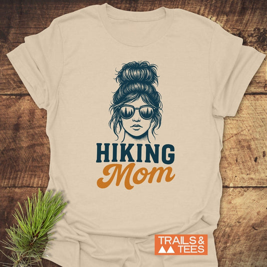 Messy Bun Hiking Mom T-Shirt featuring a line drawing of a woman with a bun and forest-reflecting sunglasses, emphasizing comfort and adventure-ready design.