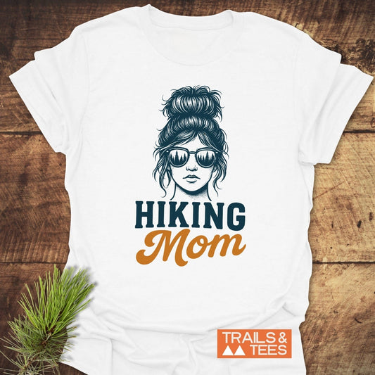 Messy Bun Hiking Mom T-Shirt featuring line-art of woman with forest-reflecting sunglasses and HIKING Mom text, crafted from soft, lightweight cotton with durable prints.