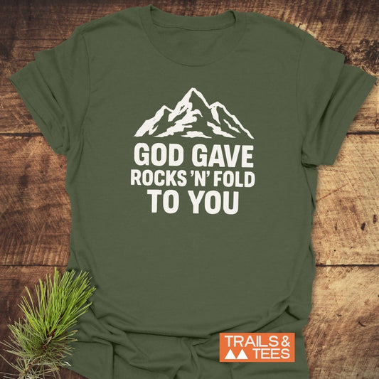 Olive-green God Gave... Funny Geology T-Shirt featuring a mountain graphic and text, with an orange TRAILS & TEES logo, on a wooden surface.