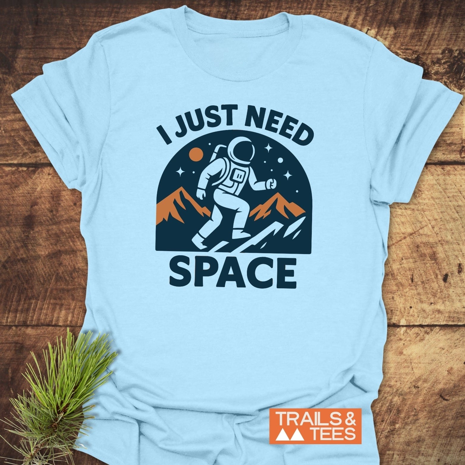 Pale-blue I Just Need Space T-shirt with astronaut graphic, rust/orange mountains, and starry sky. Ideal for outdoor enthusiasts, crafted from soft, durable cotton.