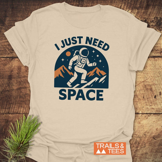 I Just Need Space T-Shirt featuring an astronaut graphic on a light-beige tee, highlighting comfort and durability with Trails & Tees branding.