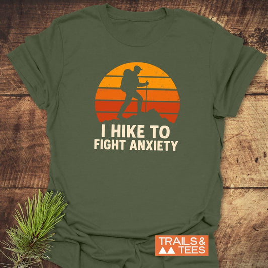 Olive-green Hike To Fight Anxiety T-shirt featuring a hiker graphic against a vintage sunset, crafted from soft cotton for comfort and durability.