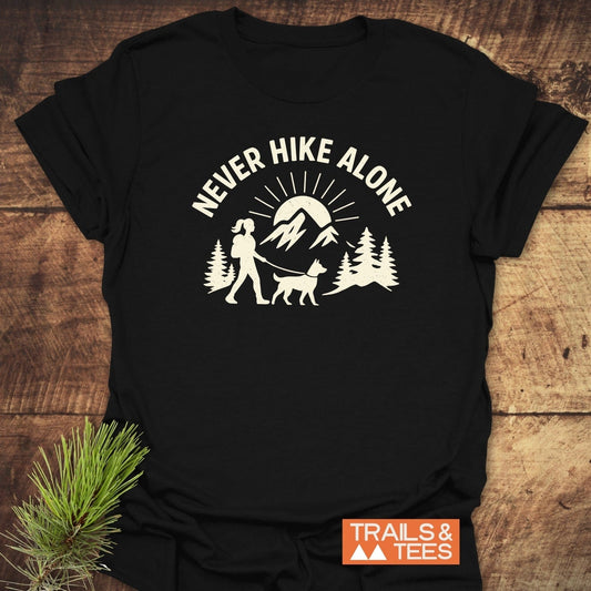 Never Hike Alone Dog Mom T-Shirt with hiker and dog graphic, crafted from soft cotton, featuring durable print for outdoor enthusiasts.