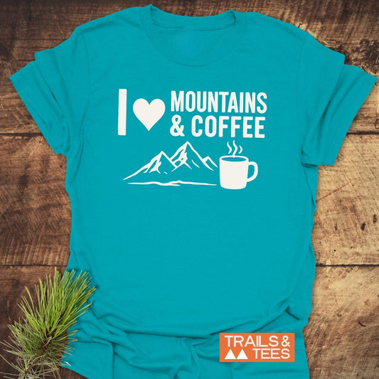 Teal T-shirt with I ♥ Mountains & Coffee slogan, featuring mountains and a coffee mug graphic. Includes TRAILS & TEES logo.