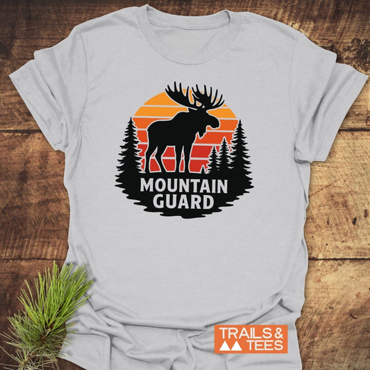 Mountain Guard Moose T-Shirt on wood, featuring a moose and pine tree graphic with TRAILS & TEES logo, highlighting outdoor adventure and durability.