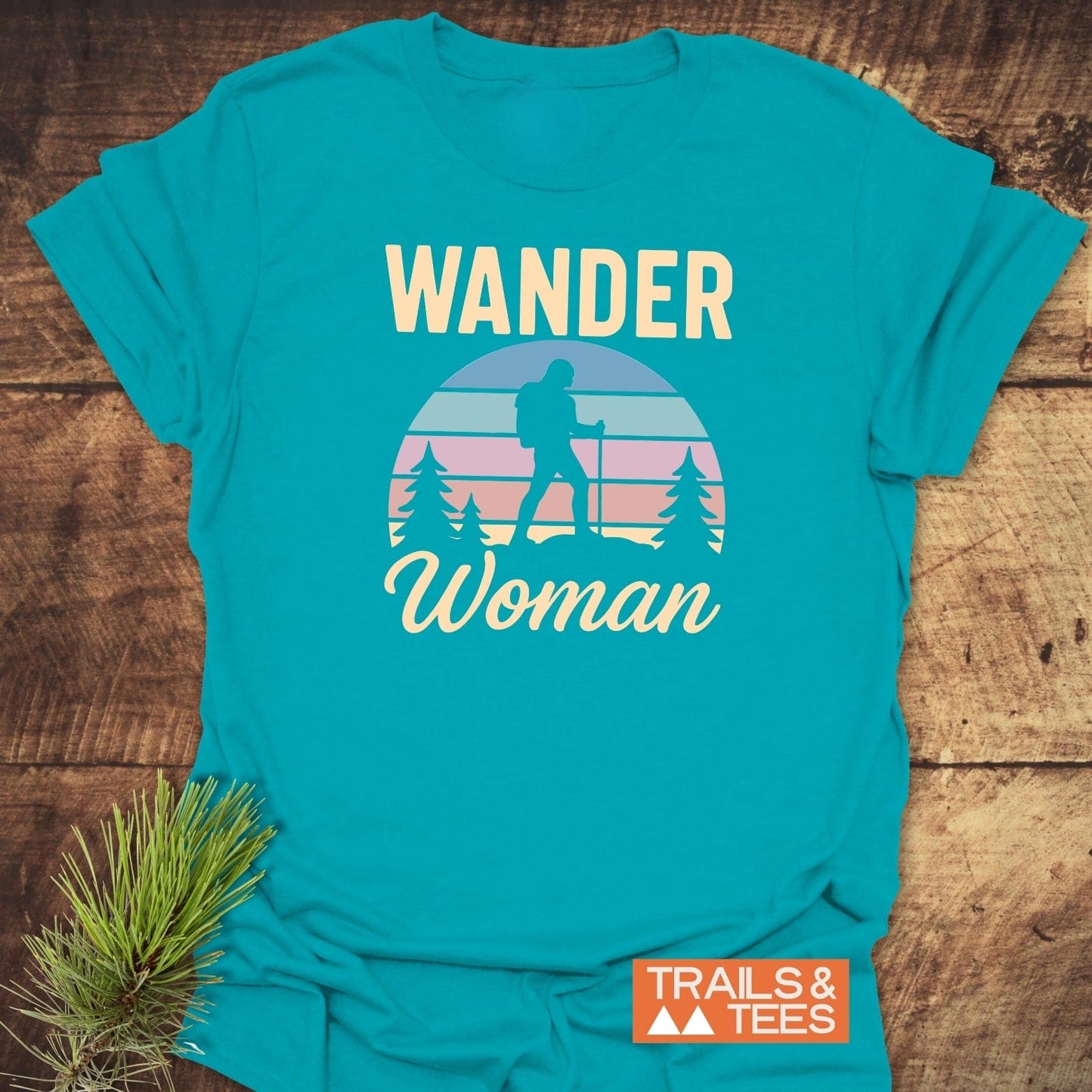 Wander Woman Retro T-Shirt: Turquoise tee with a female hiker silhouette, evergreen trees, striped sky graphic, WANDER Woman text. Includes TRAILS & TEES logo.