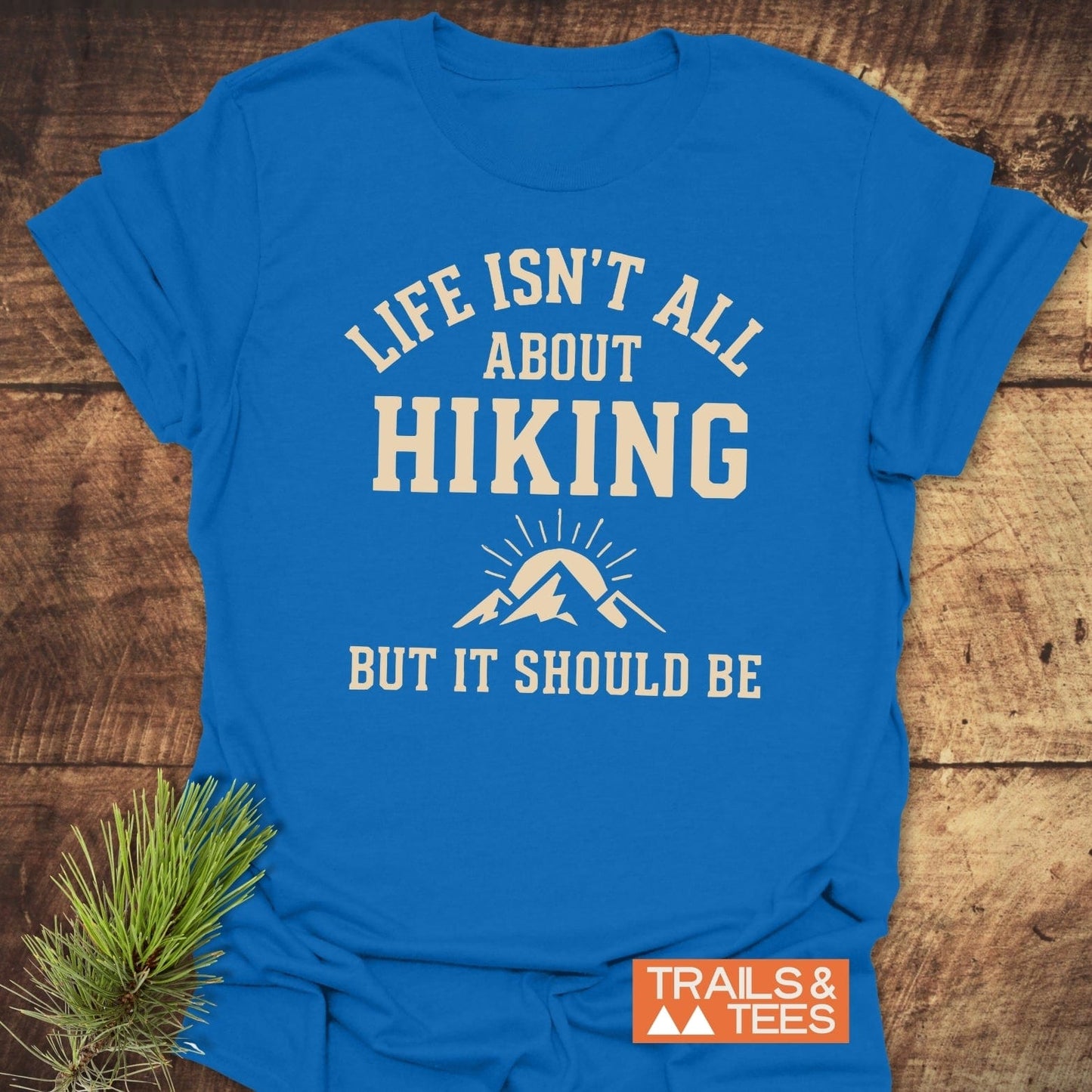 Life Isn't All About Hiking T-Shirt with cream graphic, laid on wood. Features soft cotton, durable print, taped shoulders, no side seams, eco-friendly on-demand print.