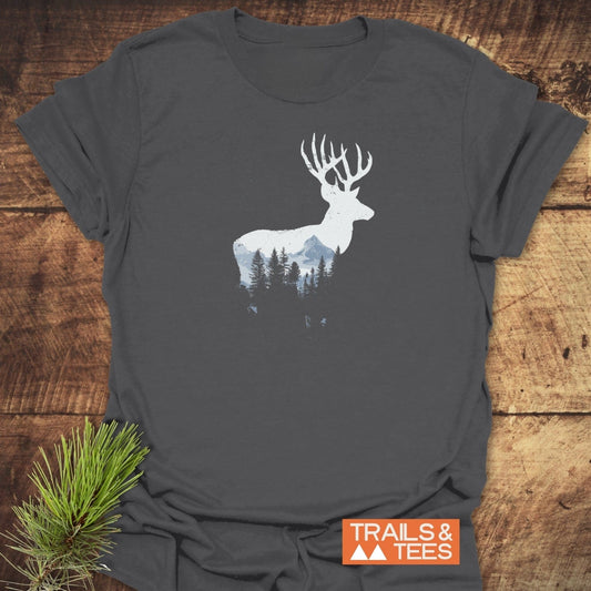 Deer Silhouette T-Shirt on rustic wood, featuring a forest and mountain design in white. Includes TRAILS & TEES logo, emphasizing comfort and outdoor style.