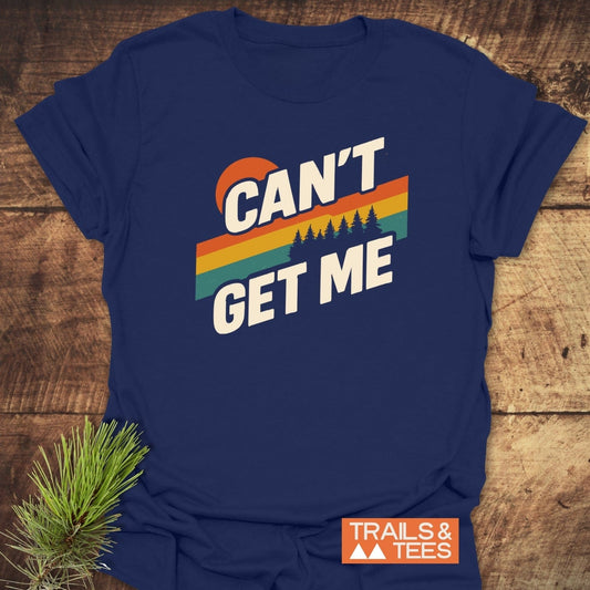 Can't Get Me Hiking T-Shirt featuring a retro graphic with sun, stripes, and trees, laid on wood. Includes “TRAILS & TEES” badge and pine branch.