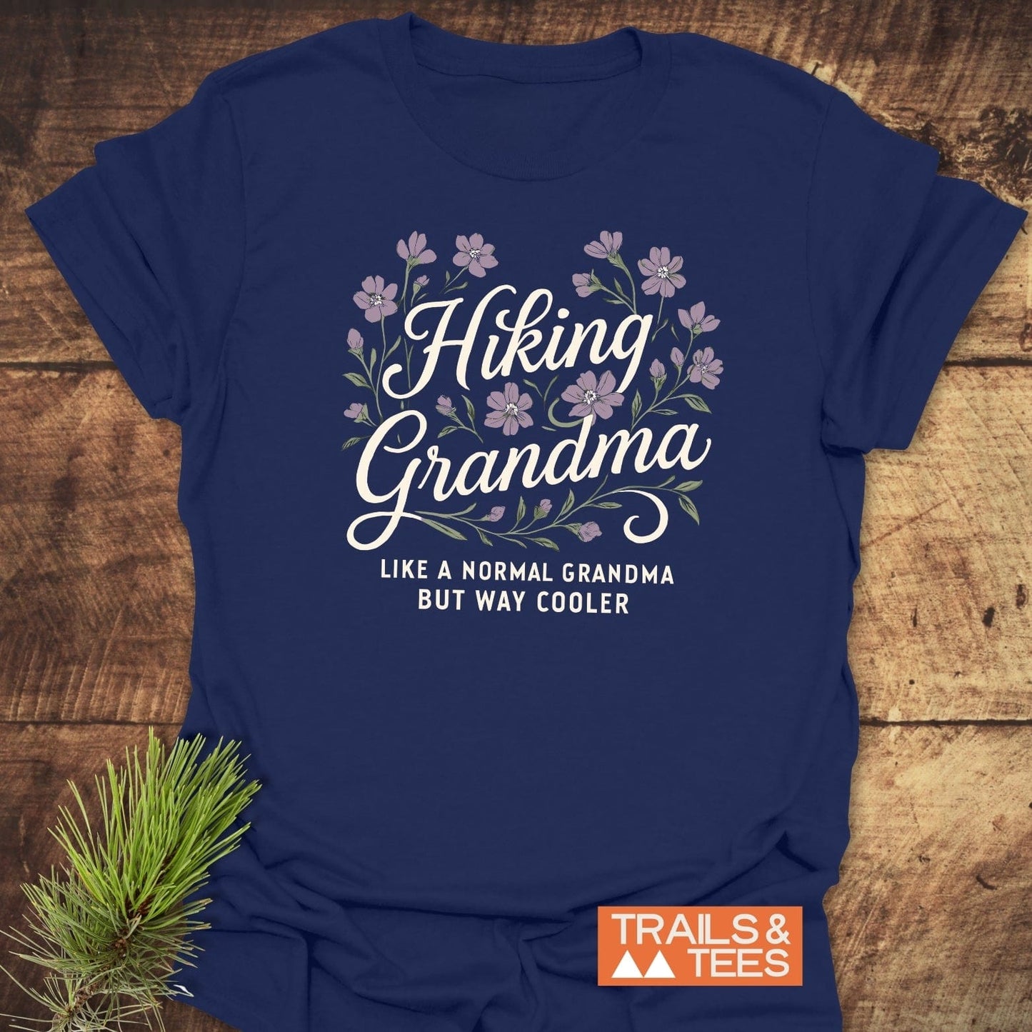Navy blue Hiking Grandma T-shirt with purple floral wreath graphic, highlighting adventurous spirit. Made of soft, durable cotton for outdoor comfort.