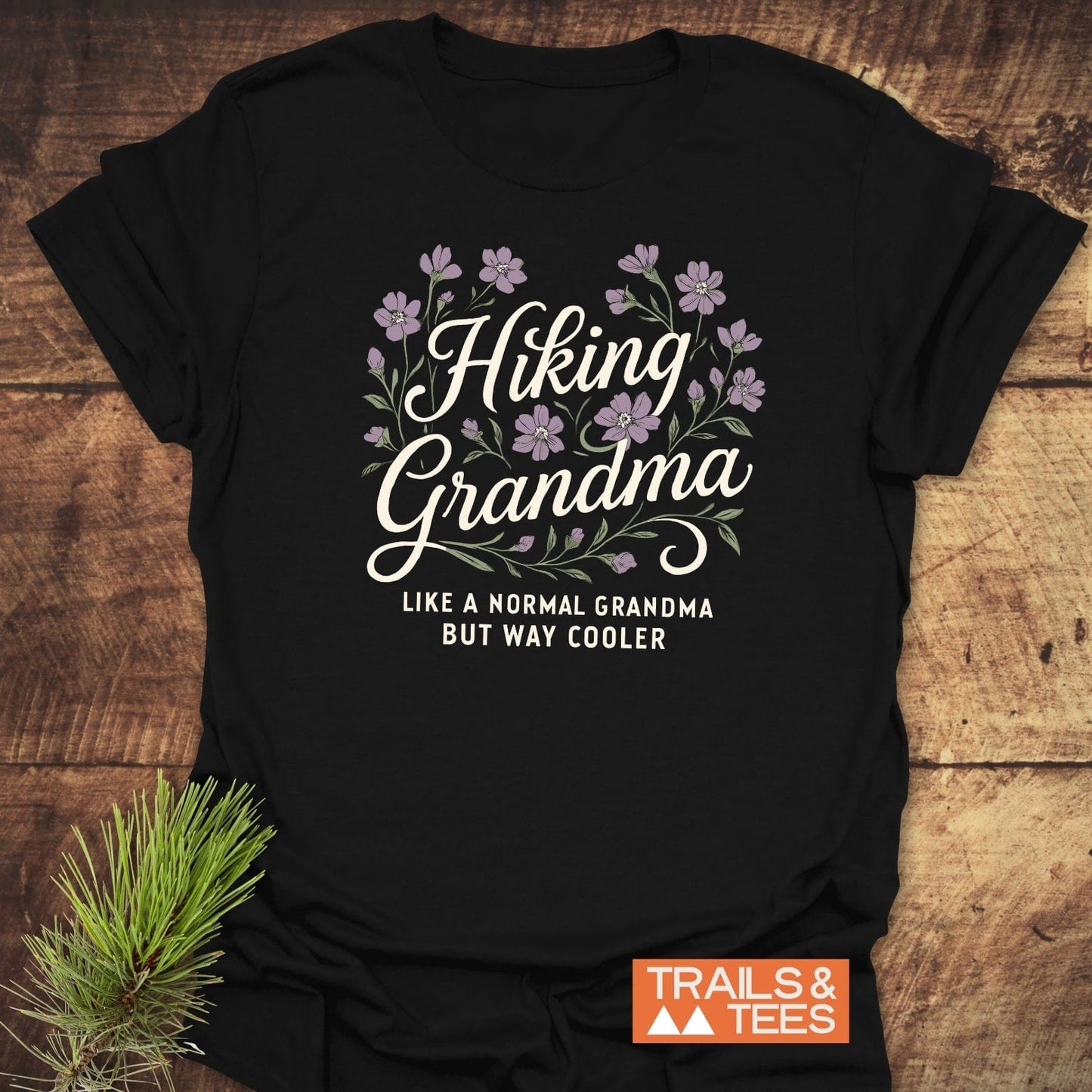 Hiking Grandma Floral T-Shirt on wooden surface with evergreen sprig; features floral graphic and Like a normal grandma but way cooler text.